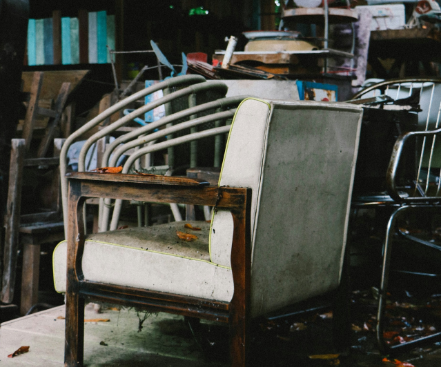 Old and damaged furniture, including chairs and a worn-out armchair, in a cluttered storage space.