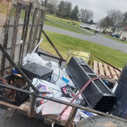 Trailer filled with junk, including electronics, metal parts, and bags of trash, ready for removal at a residential area.