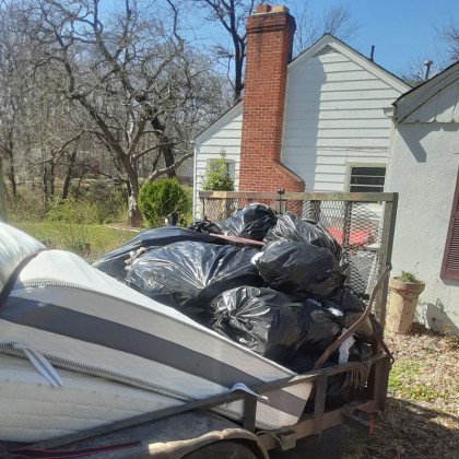 Trailer loaded with black garbage bags and old mattresses for junk removal by Tom's Junk Services.